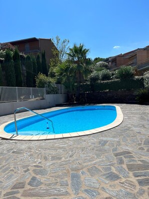 Relax by the clear blue pool surrounded by lush greenery and a stone patio.