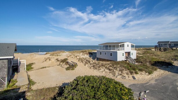 Ein Strandhaus mit großzügigem Balkon mit Blick aufs Meer, gelegen auf Sanddünen und mit freiem Blick auf die See.
