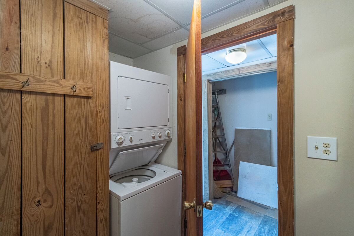Lavanderia con lavatrice e asciugatrice, mobili impiallacciati in legno e una porta che dà su un'altra stanza.