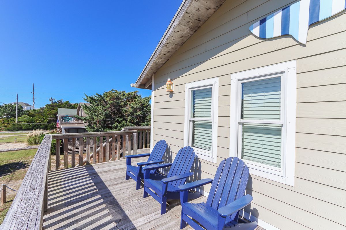 A wooden deck with three blue chairs, a railing, and a house with white shutters.