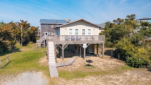 A house with a wooden deck, a staircase, and a sandy yard. - Pet-friendly oceanside Hatteras Island home by Sun Realty (Avon)