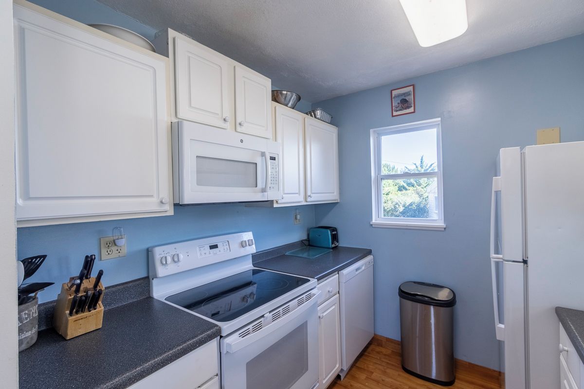 A compact kitchen with white cabinets, a microwave, a stove, a dishwasher, and a trash bin.