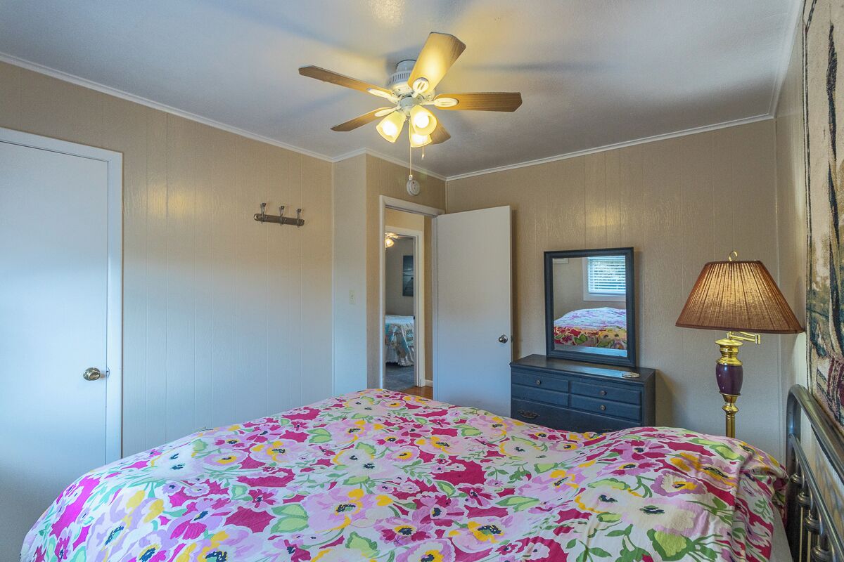 A bedroom with a bed, a ceiling fan, a dresser, a lamp, and a mirror.