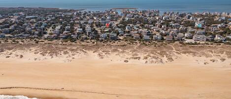 Vista aérea de una zona residencial costera con casas a lo largo de la playa, arena y el océano.