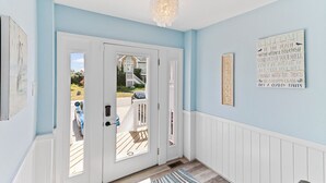 A hallway with light blue walls, white wainscoting, a double door, and a chandelier. - Sun Realty gorgeous pet-friendly oceanside home w/ pool, hot tub, & elevator! (Corolla)