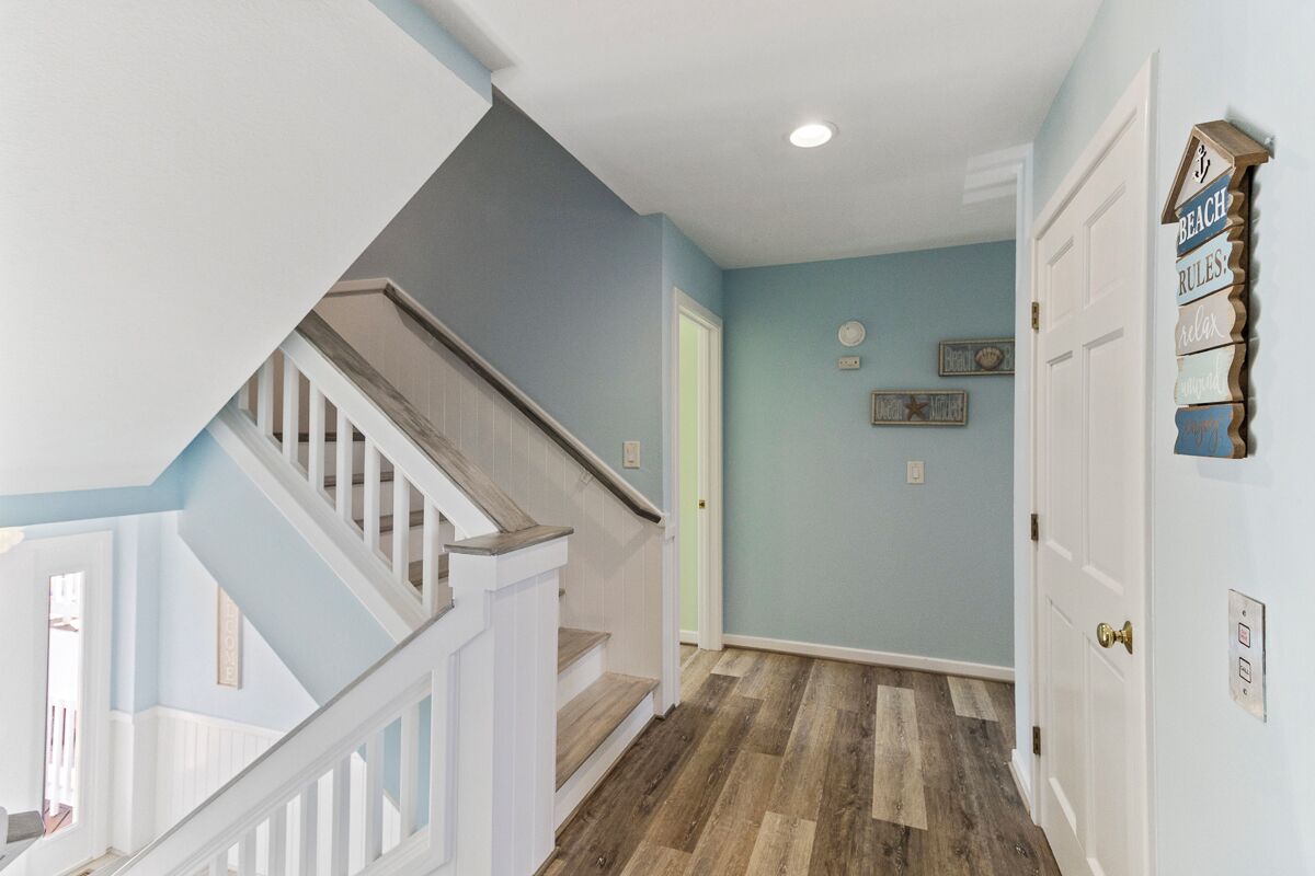 A staircase with white railings leading to a landing with a light blue wall and a wooden floor.
