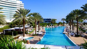 A large swimming pool with lounge chairs and palm trees, surrounded by modern buildings.