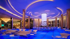 A spacious lobby with a central bar, comfortable seating, and a modern ceiling design.