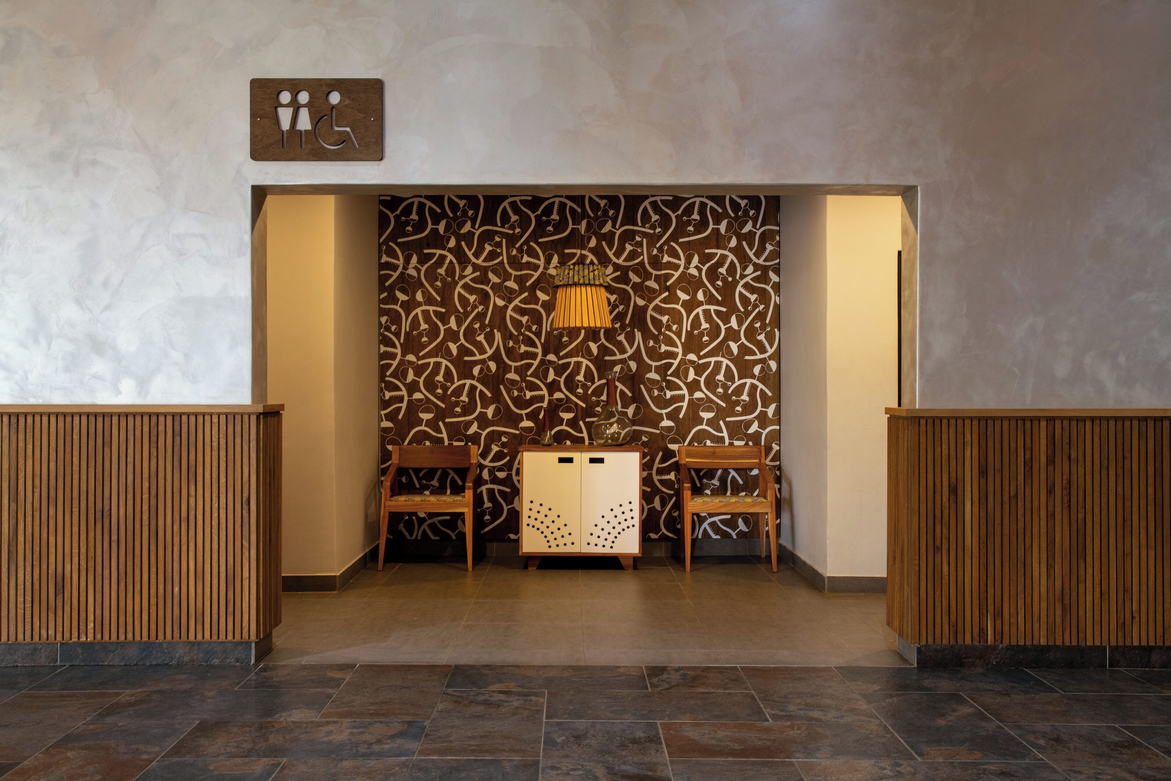 Un espace d’accueil avec un mur décoré de motifs, deux bancs en bois, un meuble et un panneau indiquant que les lieux sont accessibles aux personnes à mobilité réduite.