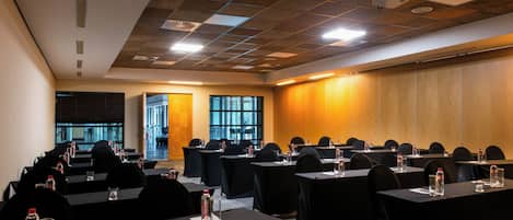 Un salón de conferencias con varias mesas, sillas y un panel de pared de madera.