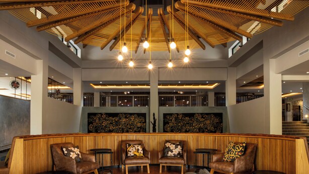 A lobby with a wooden reception desk, leather chairs, a fur rug, and a high ceiling with hanging lights.