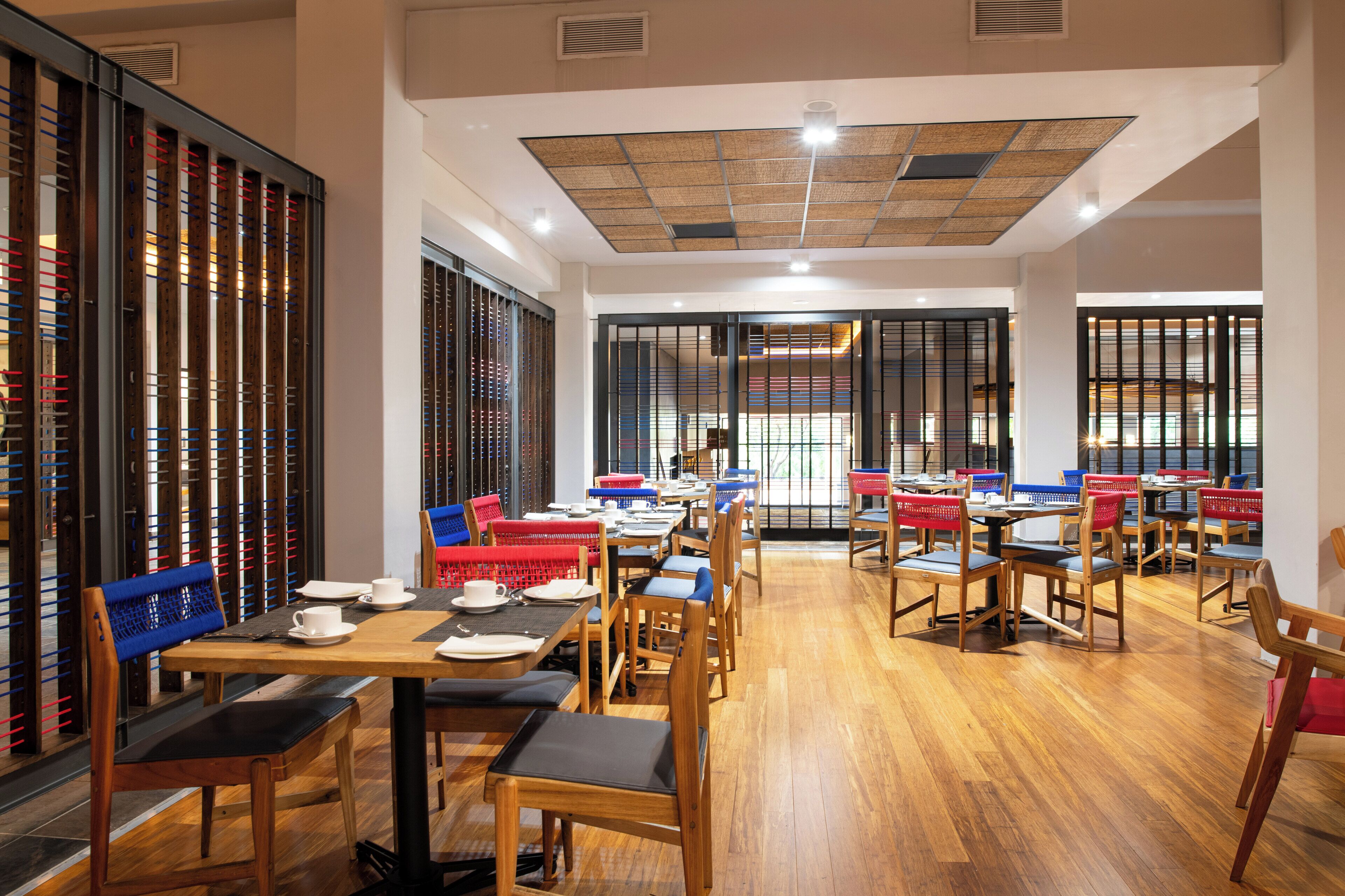A restaurant with wooden tables and chairs, a tiled ceiling, and large windows.