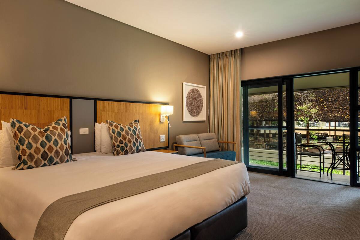 A modern hotel room with a large bed, a desk, and a view of the outdoors.