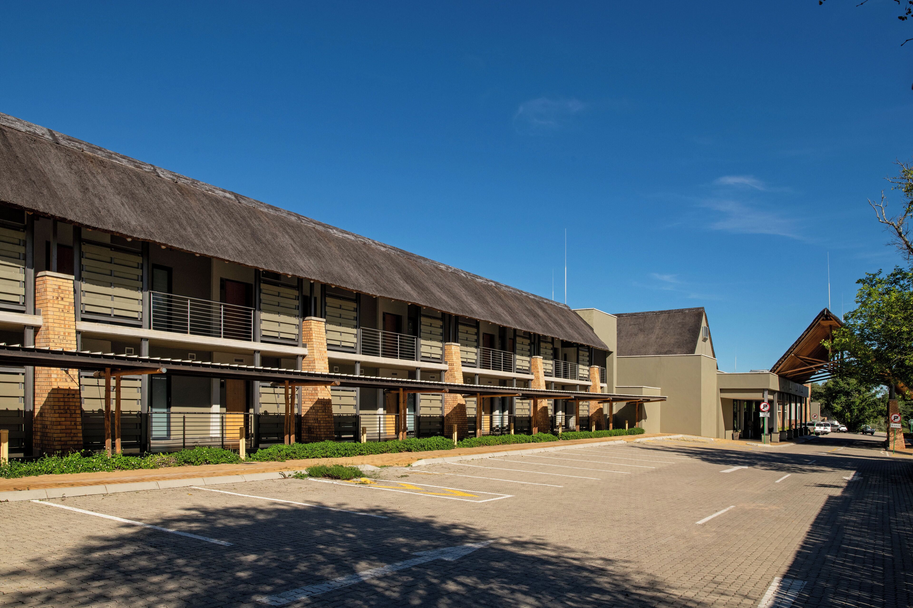 A modern hotel with a covered outdoor area, a parking lot, and a clear blue sky.