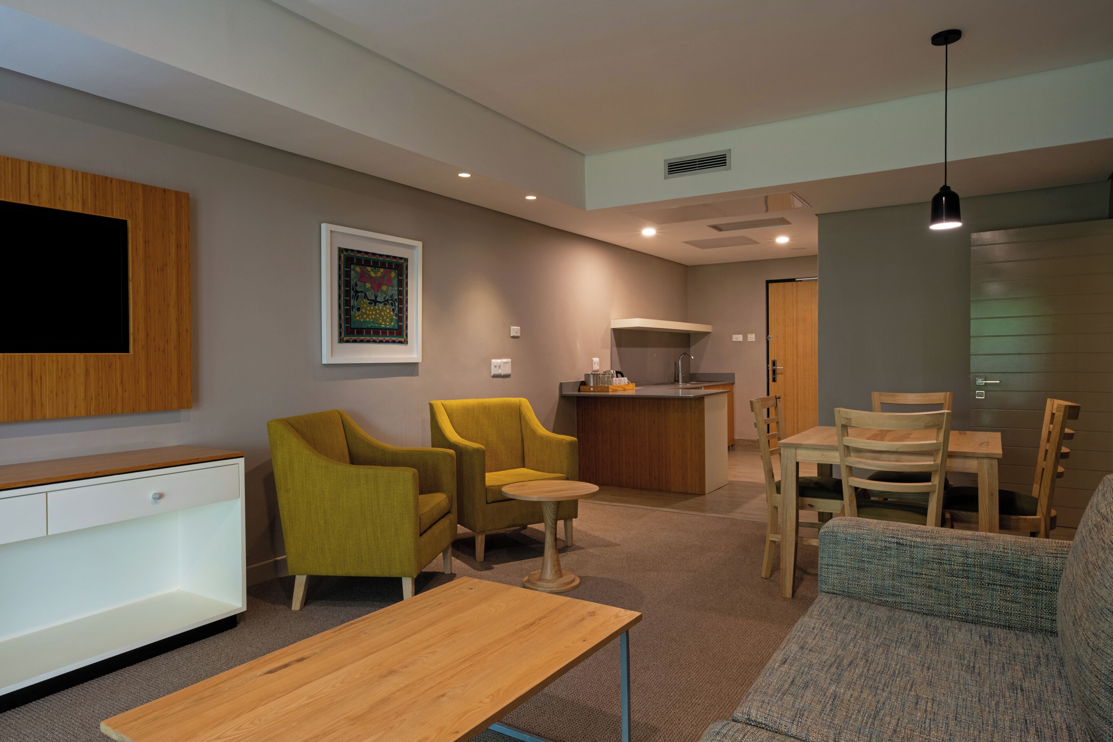 A modern living room with a sofa, two armchairs, a wooden coffee table, a small round table, and a kitchen area in the background.