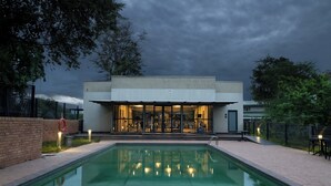 A modern building with a swimming pool in front, featuring a glass facade and outdoor seating area.