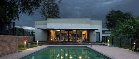 Un edificio moderno con piscina frente a él, que cuenta con fachada de vidrio y zona de estar al aire libre.