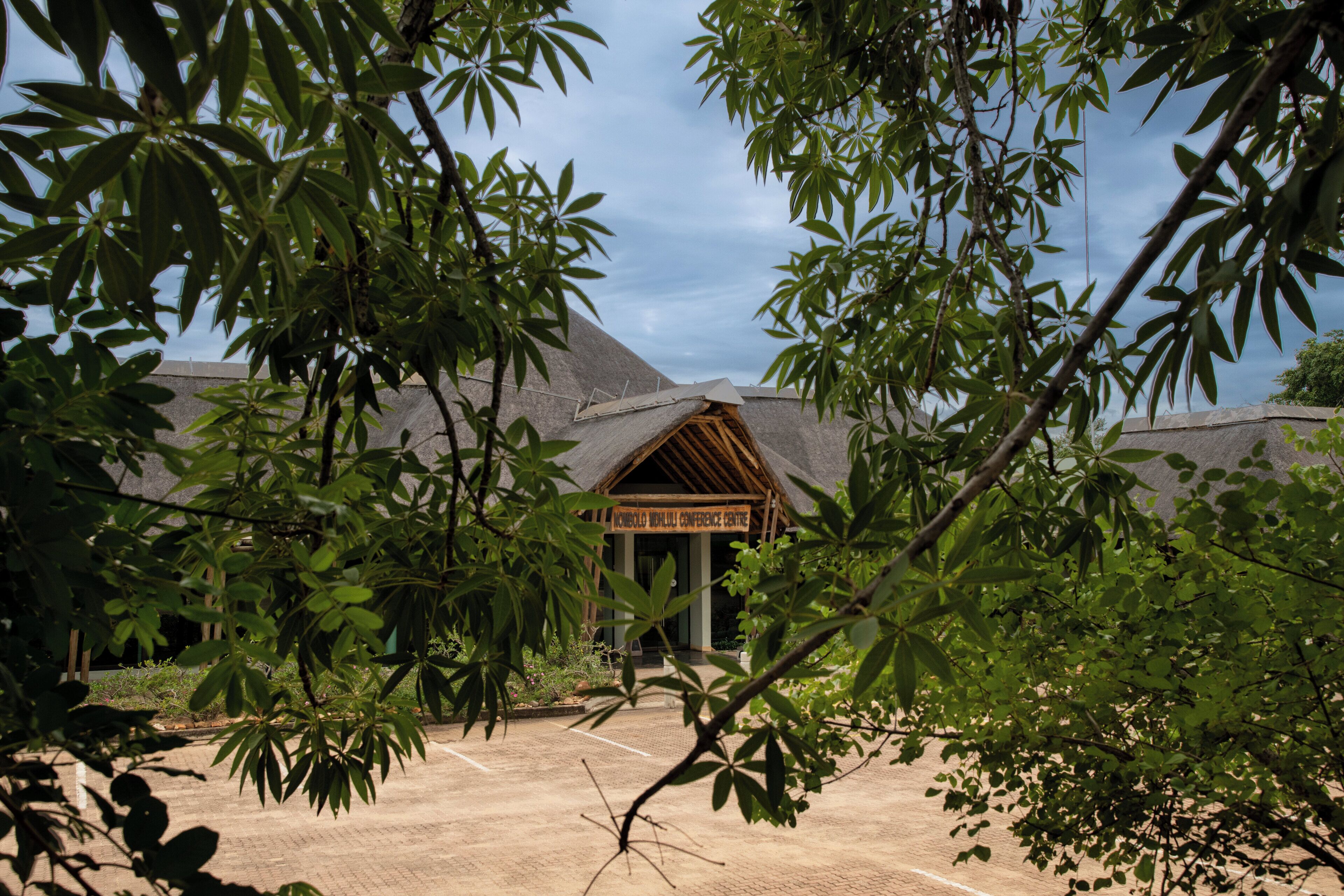 A conference center with a thatched roof, surrounded by lush greenery.
