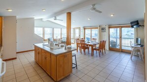 Una cocina amplia con una isla central, comedor con sillas y un balcón con televisor.