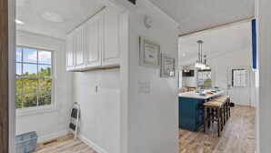 Cucina con mobili bianchi, un'isola centrale con sgabelli, una grande finestra e certificati incorniciati alle pareti.
