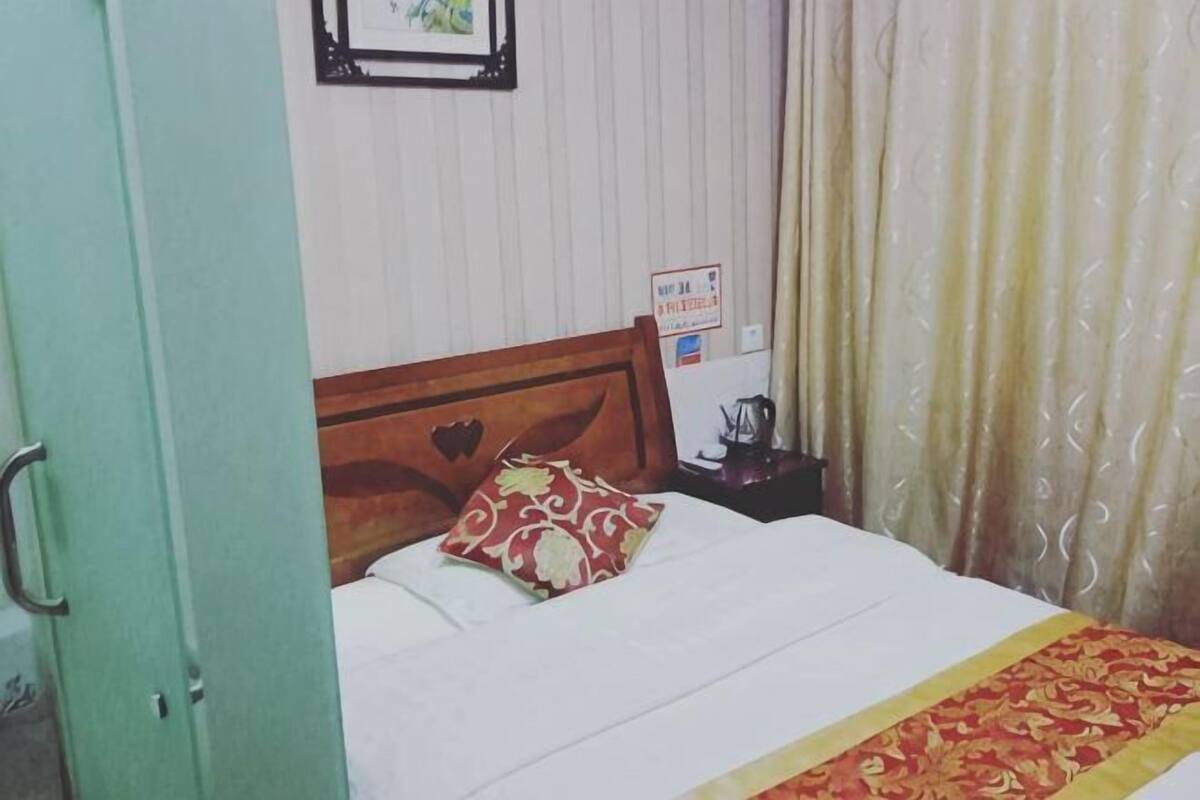 A bed with a wooden headboard, a red patterned pillow, and a white bedspread.
