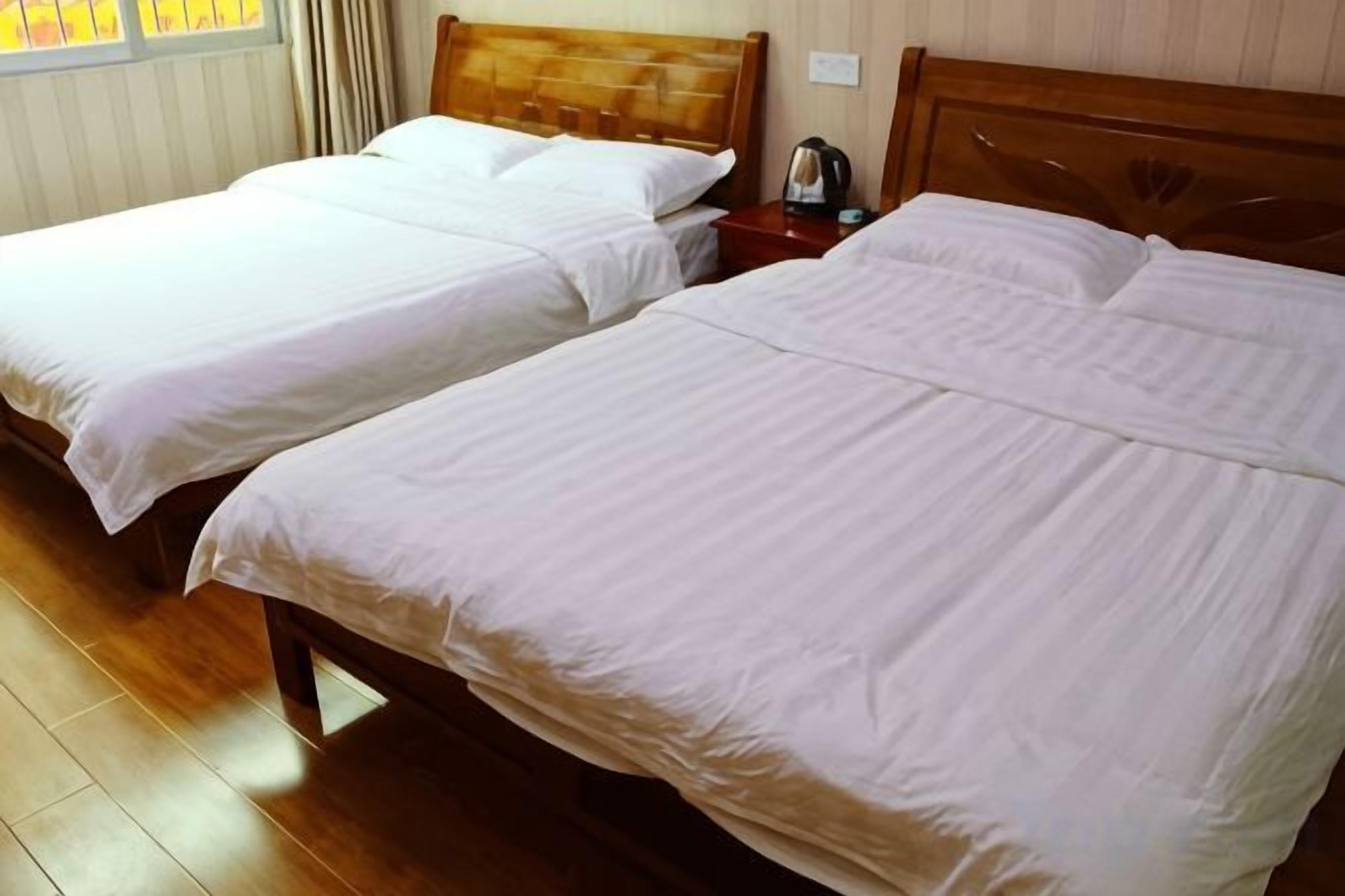 Two single beds with wooden frames and white linens in a room with wooden flooring.