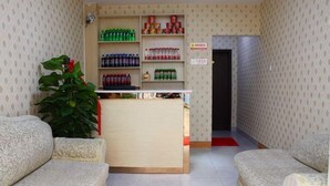 A reception area with a desk, two sofas, a potted plant, and shelves stocked with beverages. - Hefei Ruyi Inn (Hefei)