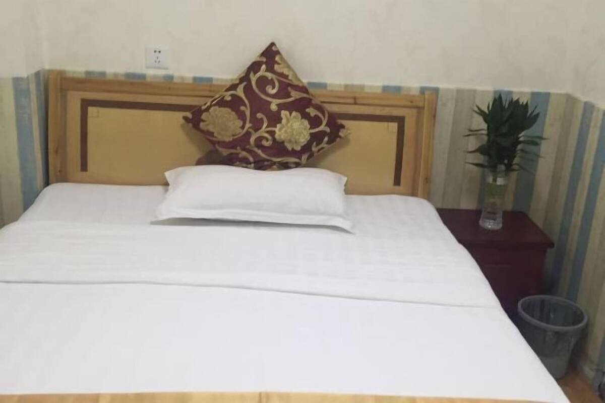 A bed with a wooden headboard, a single white pillow, and a decorative pillow with a floral pattern.