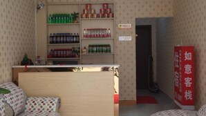 A hotel room with a bed, a small desk, a shelf with beverages, and a red sign.