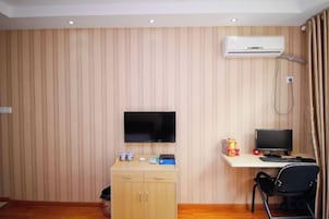 Una habitación con pared de paneles de madera, un televisor de pantalla plana montado sobre un mueble de madera, un escritorio con una computadora y una silla.