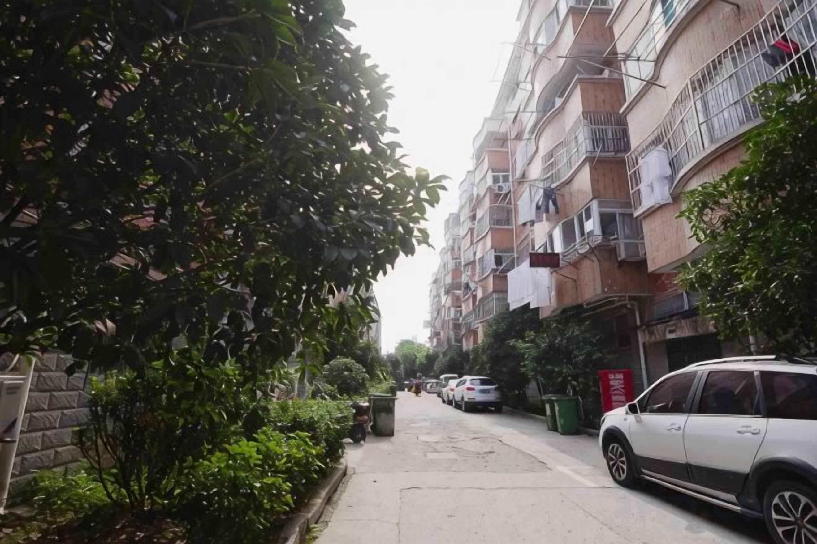 A residential street with multi-story buildings, parked cars, and a sidewalk.