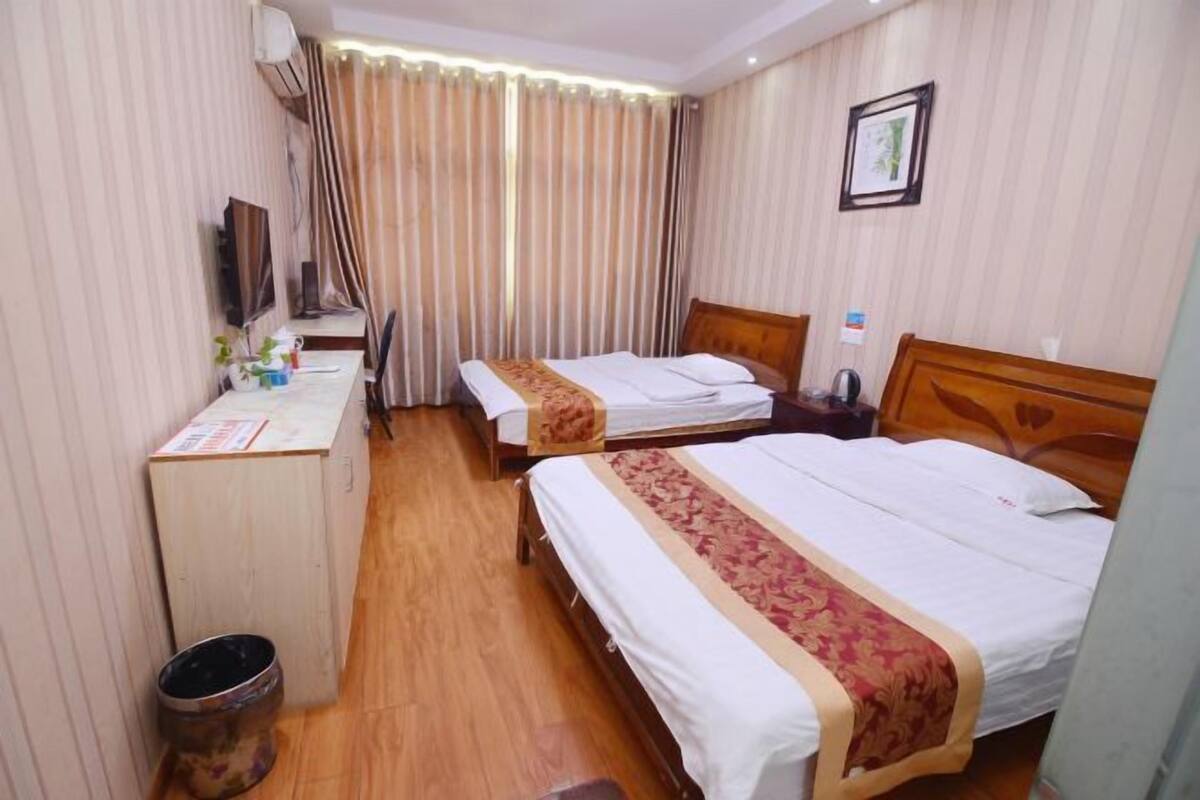 A hotel room with two beds, a desk, a chair, a TV, and a curtain.