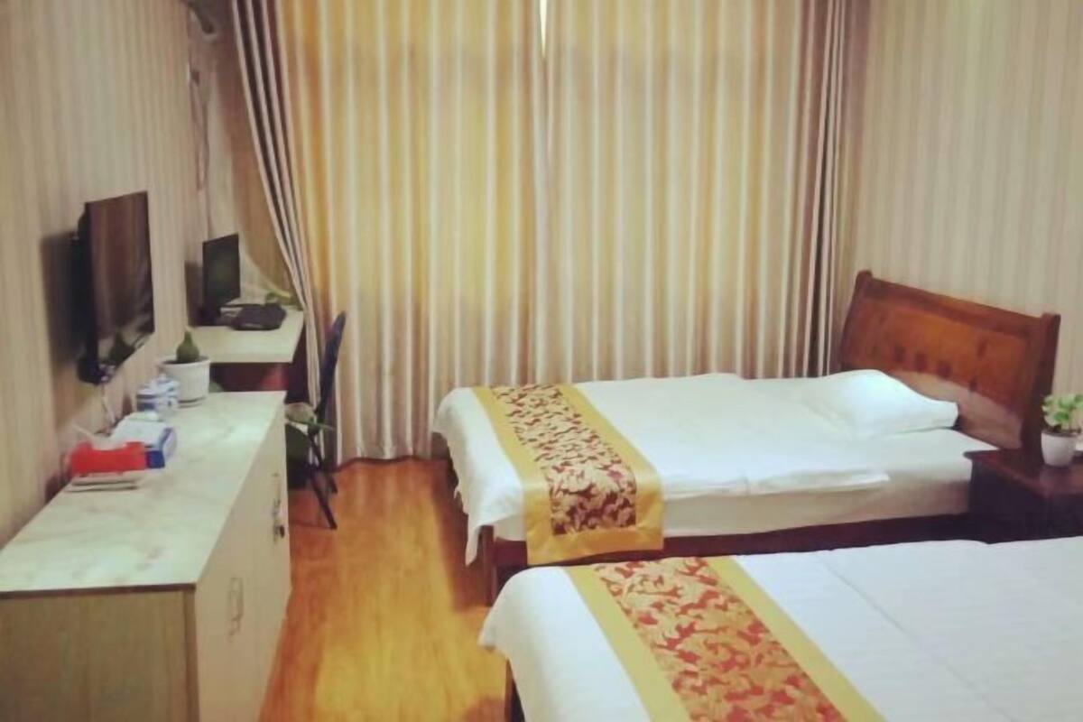 A hotel room with two beds, a desk, a television, and a curtain.