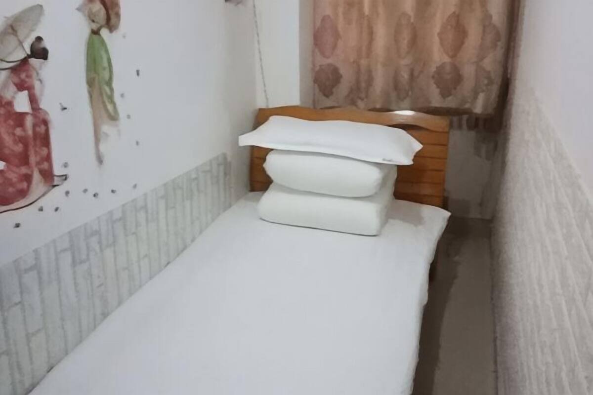 A narrow room with a wooden bed, white bedding, and a wall with a partial view of a person.