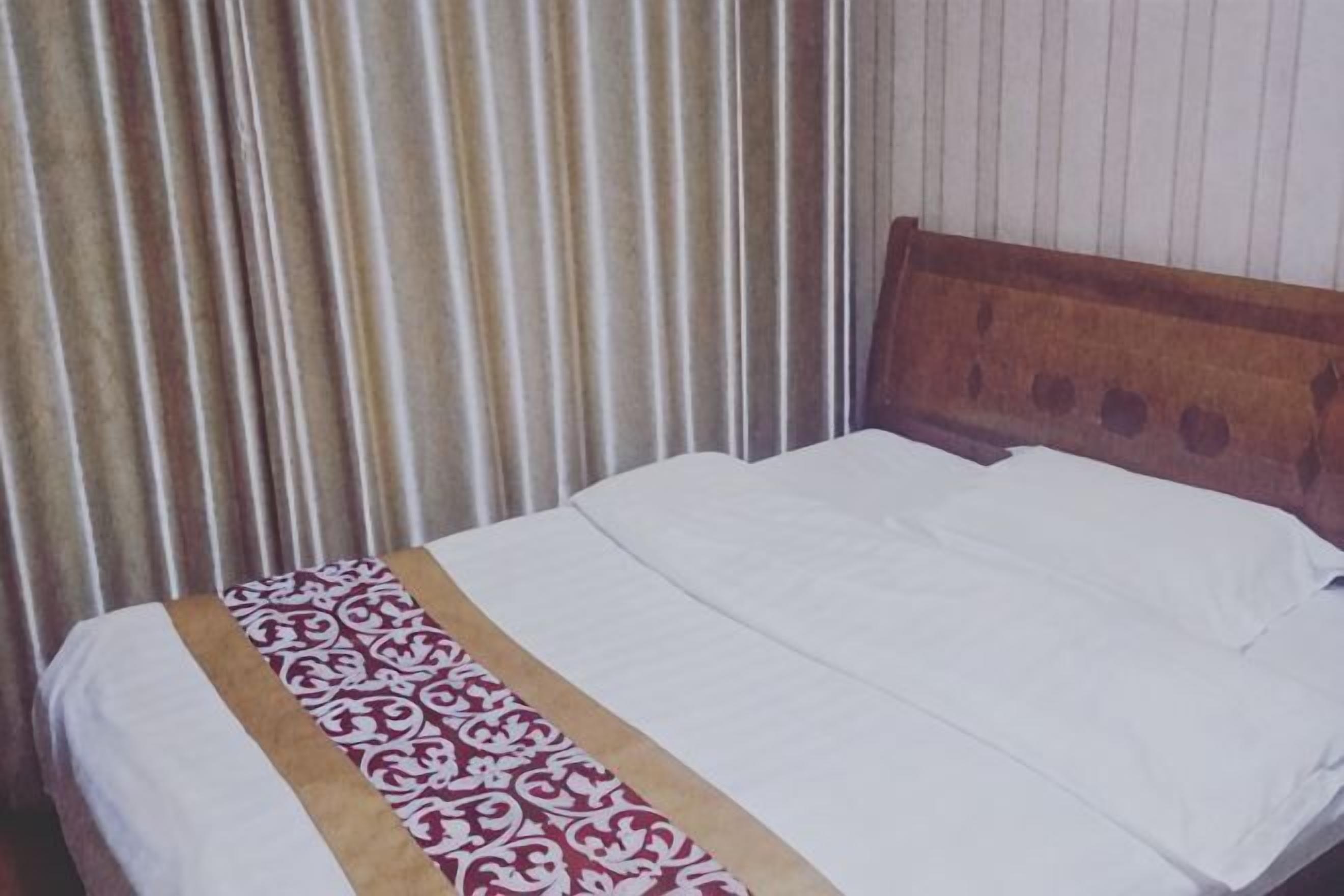 Uma cama com cabeceira de madeira, colcha estampada e cortina listrada.