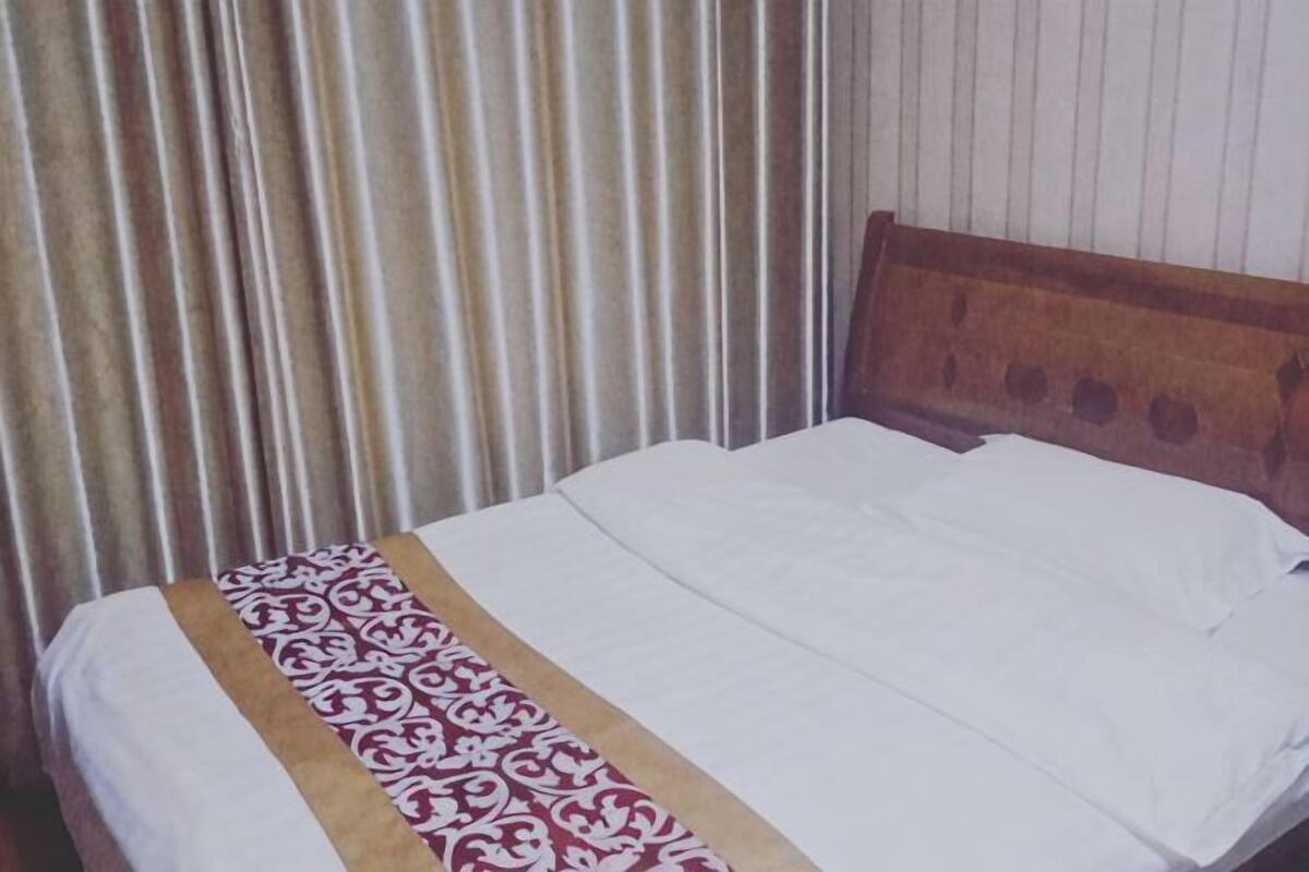 A bed with a wooden headboard, a patterned bedspread, and a striped curtain.