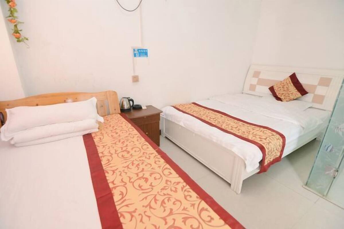 A hotel room with two beds, a wooden headboard, a bedside table with a kettle, and a wall-mounted sign.