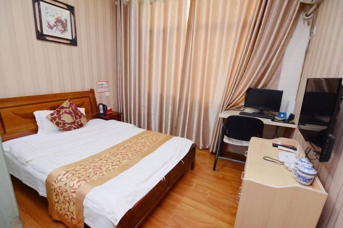 A hotel room with a wooden bed, a desk with a computer, and a television.