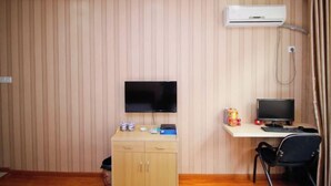 A room with a wooden paneled wall, a mounted flat-screen TV, a desk with a computer, a chair, and a small cabinet with items on top. - Hefei Ruyi Inn (Hefei)