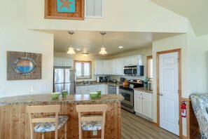 Una cocina con una isla central, sillas de madera, armarios blancos y un refrigerador de acero inoxidable.