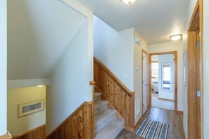 Ein Flur mit einer Holztreppe, einer Tür zu einem Zimmer und einer Wandleuchte.