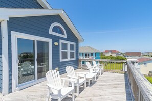 A blue building with a covered deck, white chairs, and a view of other houses.