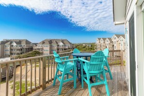 A balcony with a view of residential buildings, a wooden deck, and turquoise chairs.