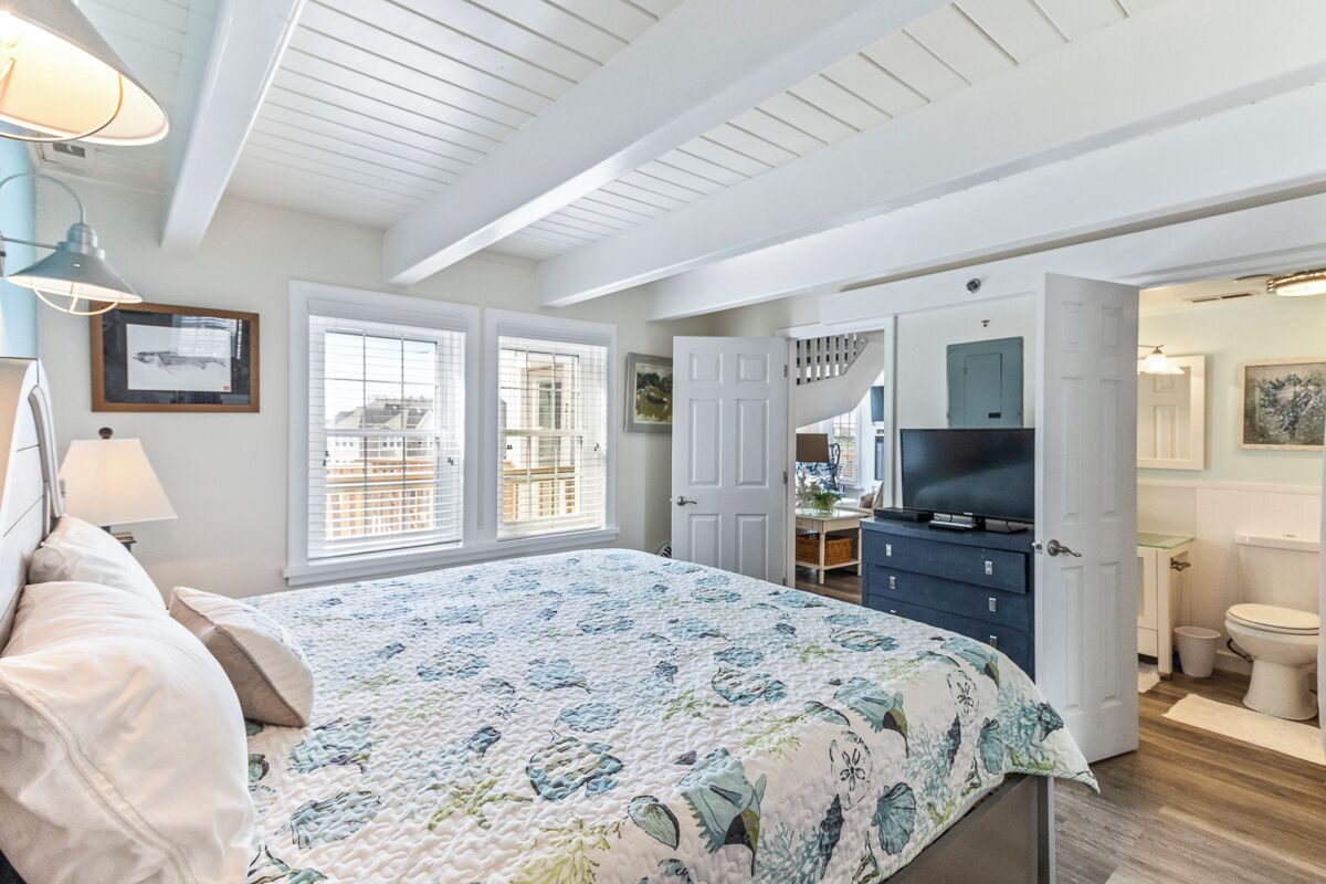 Un dormitorio con cama, cómoda, televisor y baño visible a través de una puerta abierta.