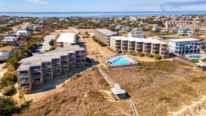 Vue aérienne d’un quartier résidentiel situé sur la côte, avec plusieurs immeubles d’appartements, une piscine et une plage.