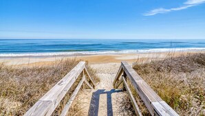 Une promenade en bois qui mène à une plage, avec un ciel bleu dégagé.