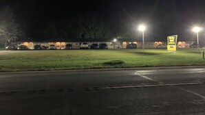 Un parking avec plusieurs voitures et un bâtiment dont les fenêtres sont illuminées.