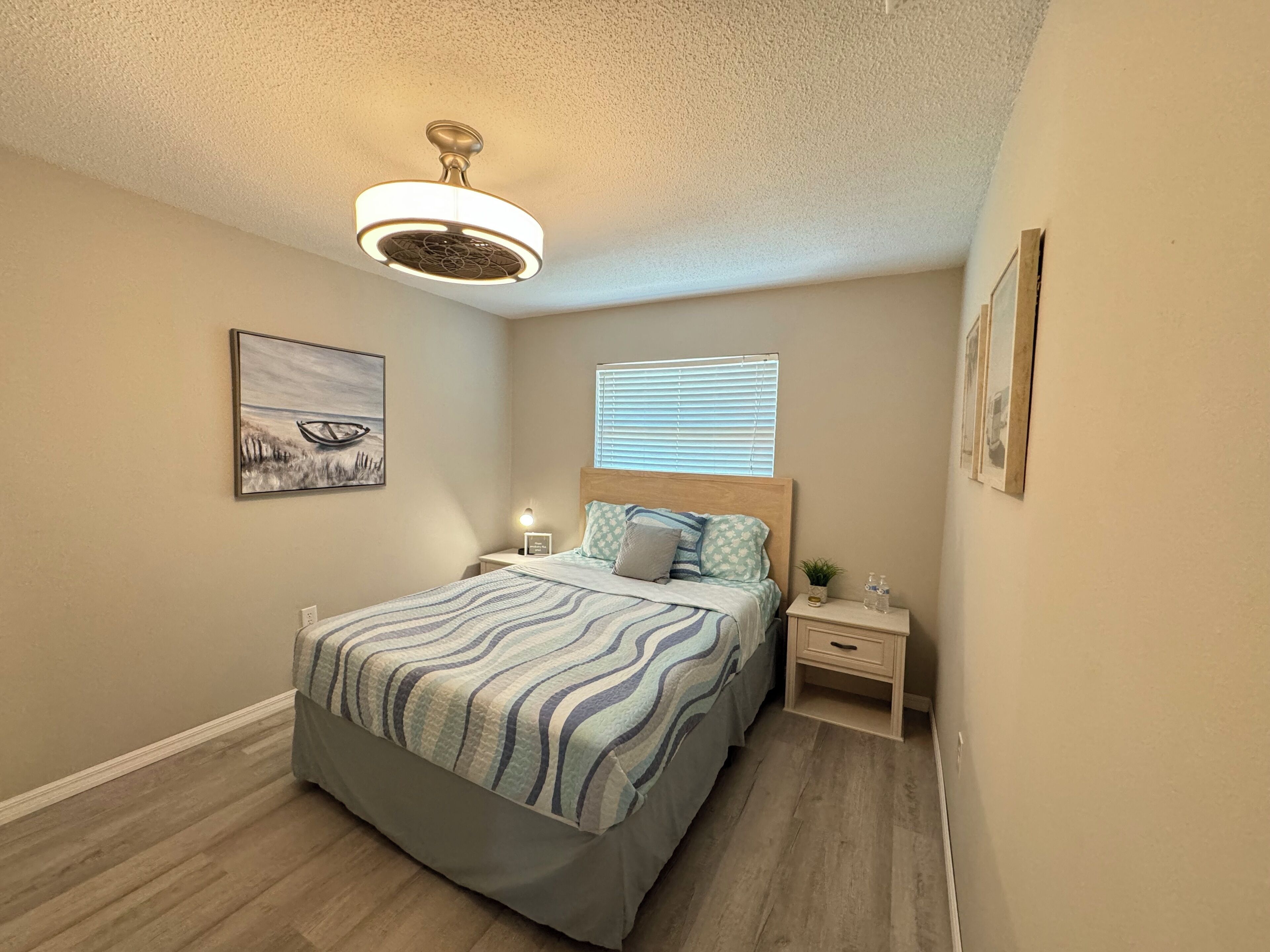 A bedroom with a bed, nightstands, a ceiling fan, and a window with blinds.
