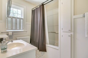 Un baño con un lavamanos blanco, una ventana con persianas, una cortina de ducha y un perchero para toallas.