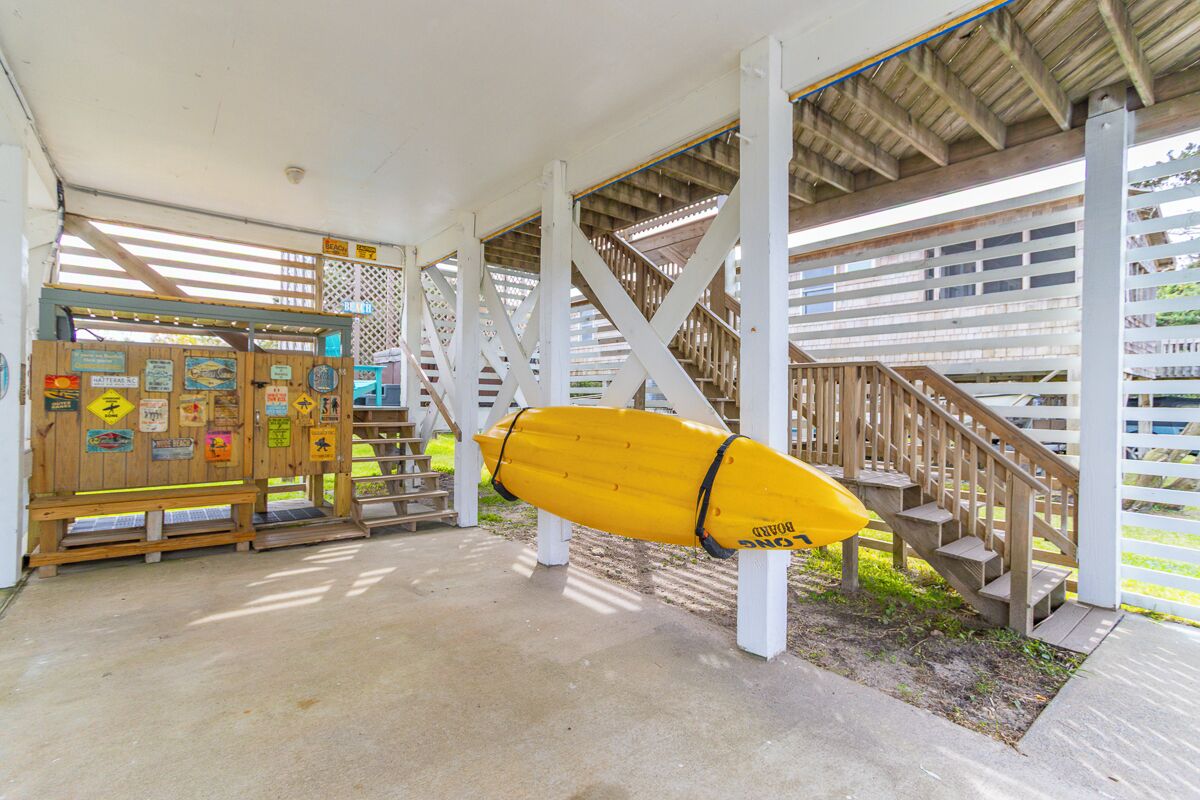 A covered area with a lifeguard stand, a yellow surfboard, and a staircase.